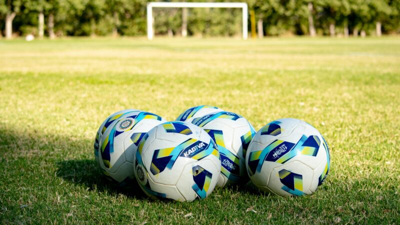 Five soccer balls rest on a green field, ready for a game in Mendoza, Argentina.